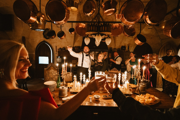 Guests raising glasses at a candlelit dinner in the château kitchen